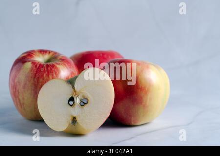 Un primo piano di mele rosse e gialle fresche, con un taglio a metà che rivela il nucleo, disposte su una superficie luminosa e moderna Foto Stock