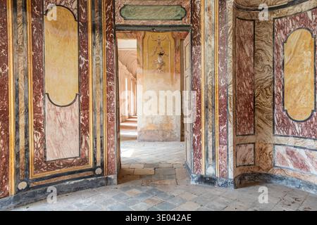AGLIÈ, ITALIA – OTTOBRE 2025: Vista interna del castello di Agliè con pareti dipinte ornate, marmi invecchiati e porte che conducono a un corrido illuminato dal sole Foto Stock