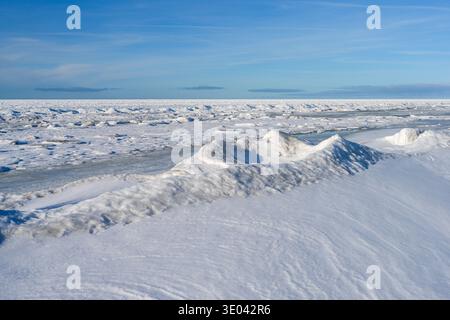 Costa ghiacciata del Mar Baltico con neve e onde ghiacciate che si estendono all'orizzonte in una giornata invernale brillante Foto Stock