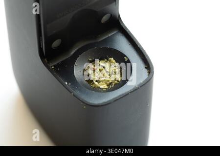 Erba di cannabis caricata in una camera di vaporizzazione secca alle erbe, dettaglio macro del dispositivo nero portatile vape con marijuana macinata, cannabis medica e gamba Foto Stock