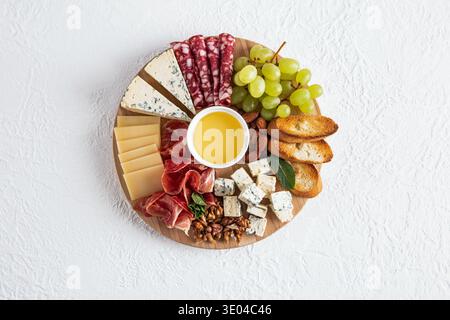 Un piatto di formaggi gourmet con un assortimento di formaggi, affettati, uva verde, mandorle, noci, e fette di pane tostato su un asse di legno, Foto Stock