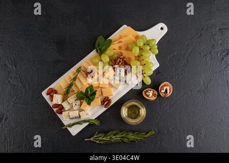 Un delizioso piatto di formaggi con una varietà di formaggi, uva verde fresca e frutta secca assortita, elegantemente disposti su un piatto da portata bianco sopra un Foto Stock