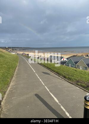 Strada costiera e passeggiata che si affaccia su Roker Beach con capanne e arcobaleno dopo la pioggia, lungomare di Sunderland, Inghilterra, Regno Unito Foto Stock