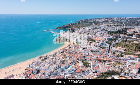 I visitatori passeggiano lungo il porticciolo di Albufeira in Portogallo. Il sole splende sul mare blu e sulla città. Molte barche sono visibili nell'area marina vicino alla riva Foto Stock