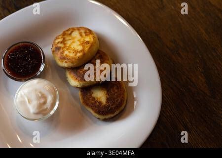 Sciroppo fatto in casa su un piatto bianco ricoperto di panna acida e marmellata di bacche dolci Foto Stock