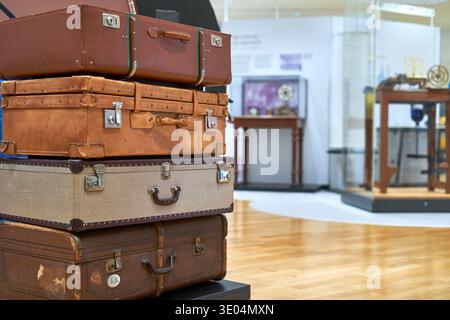 Una pila di quattro valigie vintage esposte in uno spazio espositivo del museo. I bagagli variano in dimensioni, colore e materiale, tra cui... Foto Stock
