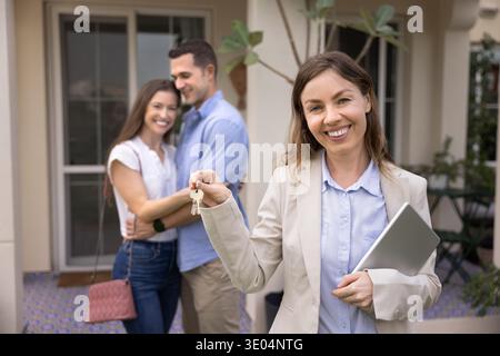 Ritratto dell'agente immobiliare che tiene le chiavi, la coppia felice sta sullo sfondo Foto Stock