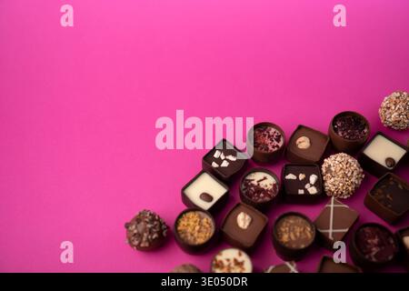 praline e tartufi di cioccolato assortiti raggruppati in basso a destra su un vibrante sfondo rosa caldo, con vari condimenti, consistenze, Foto Stock