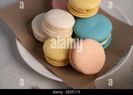 foto ravvicinata di macaron pastello impilati e disposti su un piatto bianco su pergamena marrone su un piano di legno chiaro, evidenziando la delicatezza della canna Foto Stock