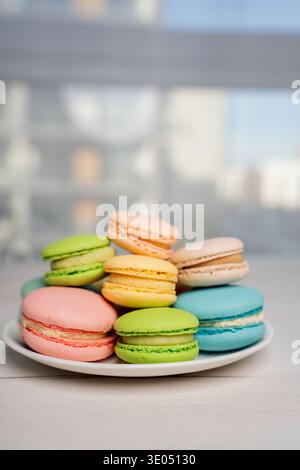 primo piano di un piatto di coloratissimi macaron pastello rosa, verde, blu, giallo e pesca impilati su un piatto di porcellana bianca su un tavolo illuminato dal sole da un blurr Foto Stock