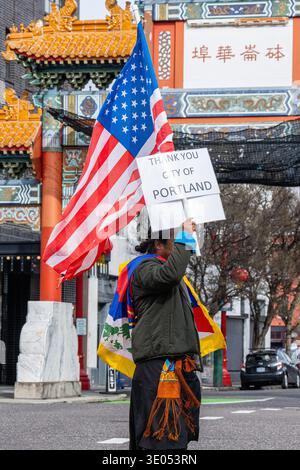 Portland, Oregon, Stati Uniti. 10 marzo 2026. Un manifestante drappeggiato con una bandiera tibetana e una sciarpa tiene una bandiera statunitense e un cartello con la scritta "Thank You City of Portland" di fronte al Chinatown Gateway in W Burnside Street durante una marcia del giorno della rivolta tibetana organizzata dalla Northwest Tibetan Cultural Association. Crediti: Norboe Photo/Alamy Live News Foto Stock