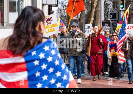 Portland, Oregon, Stati Uniti. 10 marzo 2026. Un dimostratore parla in un megafono mentre un monaco buddista cammina accanto a manifestanti portando cartelli che includono "Free the Panchen Lama" e "Tibet will be Free" durante una marcia del giorno della rivolta tibetana organizzata dall'Associazione culturale tibetana nord-occidentale in SW Morrison Street. Crediti: Norboe Photo/Alamy Live News Foto Stock