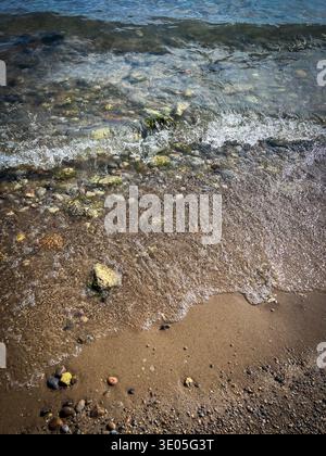 Vista ravvicinata delle piccole onde con schiuma bianca su una costa sabbiosa di ciottoli di una spiaggia dell'Ontario, Canada. Foto Stock