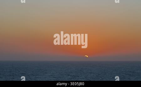 Tramonto sull'orizzonte dell'oceano con caldo cielo arancione e mare calmo che creano un tranquillo paesaggio marino. Foto Stock