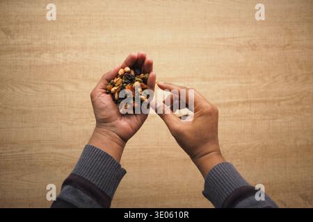 Mani che tengono in mano frutta secca e nocciole miste nella zona cucina Foto Stock