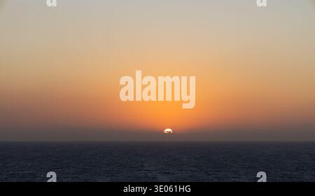 Tramonto dorato sull'orizzonte dell'oceano con caldo cielo arancione e mare calmo che creano un tranquillo paesaggio marino. Foto Stock