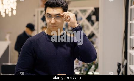 Uomo con maglione scuro che si adatta agli occhiali e sorride Foto Stock