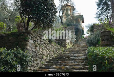 Storica scalinata in pietra che conduce alla torre gialla nel Parco di Villa Rocca. Vista prospettica di gradini rustici delimitati da tradizionali muretti a secco Foto Stock