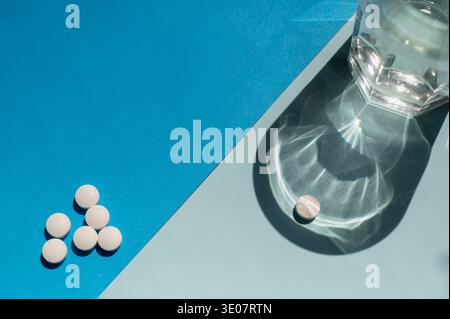 Una compressa bianca separata da un gruppo di pillole accanto a un bicchiere di acqua dolce. Concetto di aderenza alla prescrizione, prodotti farmaceutici clinici, AN Foto Stock