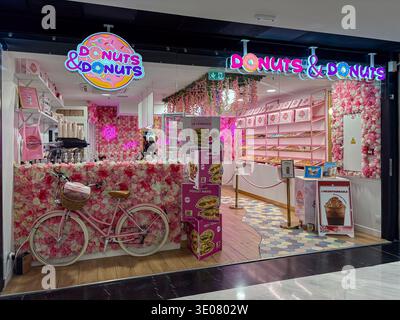 Ciambelle e ciambelle. Un vivace ingresso al negozio di ciambelle a tema rosa con pareti floreali artificiali e una bicicletta rosa in stile vintage parcheggiata all'esterno di Nizza, Foto Stock
