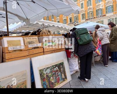 I clienti possono sfogliare stampe vintage, giornali e articoli in pelliccia in un mercato di Nizza, Francia. Edificio storico Jourdan-Gassin visibile. Foto Stock