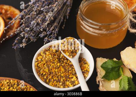 Collage di prodotti alimentari con miele, polline, zenzero ed erbe essiccate su una superficie scura Foto Stock