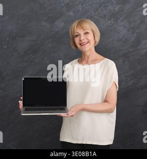 Donna sorridente che tiene un notebook con schermo vuoto per la pubblicità Foto Stock