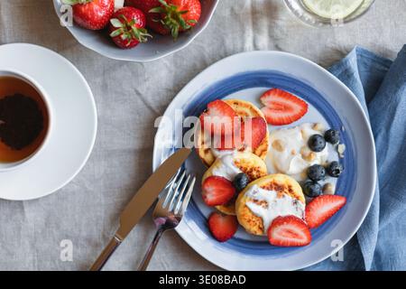 Vista dall'alto di frittelle di formaggio cottage di keto fatte in casa con fragole e mirtilli freschi, una ciotola di fragole e una tazza di tè su un tavolo Foto Stock