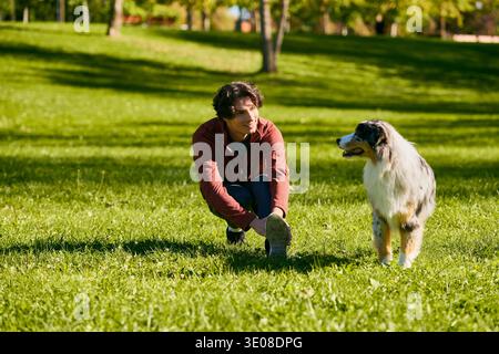 Un giovane con i capelli ricci passeggia in un parco vivace con il suo fedele pastore australiano. Foto Stock