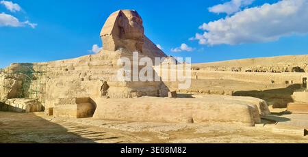 Grande statua della Sfinge presso la Necropoli di Giza sotto il cielo blu con l'antica piramide, famoso monumento egizio. Foto Stock