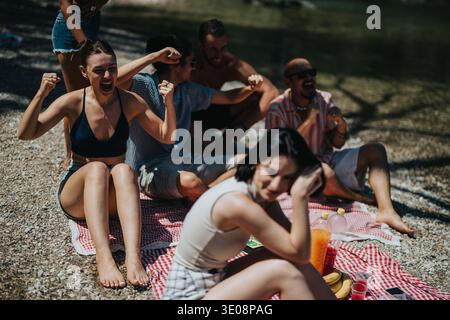Amici che si godono un picnic soleggiato sul fiume, che tifa e ride su una riva rocciosa del lago Foto Stock