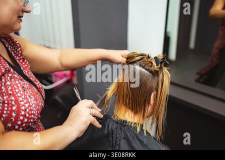 Il parrucchiere taglia i capelli biondi bagnati del cliente al salone Foto Stock