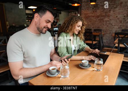 Giovane coppia che lavora su dispositivi e beve caffè al Cafe Foto Stock