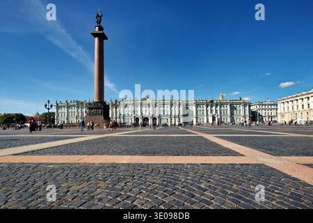 I visitatori camminano sulla piazza di fronte al Palazzo d'Inverno. La colonna Alexander si erge in alto contro il cielo blu. Foto Stock