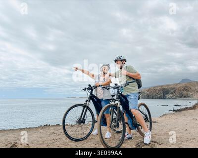 Due grandi e felici persone che si divertono e guidano in bici insieme per essere in forma e sano all'aperto. Gli anziani attivi che hanno addestramento di divertimento nella natura. Verticale Foto Stock