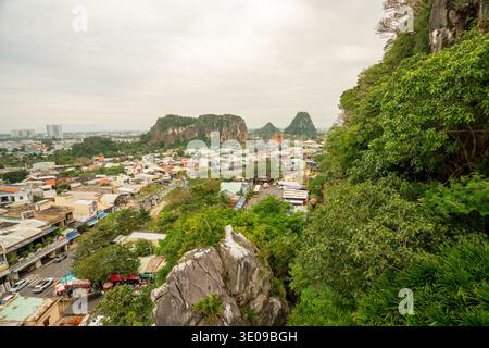 Il panorama costiero della città mostra un denso paesaggio urbano, con spettacolari formazioni carsiche calcaree e un'abbondante vegetazione tropicale sotto un cielo nuvoloso. Prodezza Foto Stock