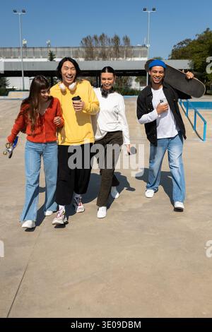 Un gruppo di quattro amici passeggia gioiosamente attraverso uno skatepark, pieno di energia e felicità. Foto Stock