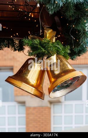 Campane natalizie dorate con nastro e ghirlanda di abete appese all'aperto Foto Stock