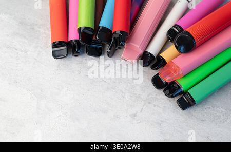 Collezione di varie sigarette elettroniche colorate monouso e penne vape sparse su sfondo grigio chiaro. Foto Stock