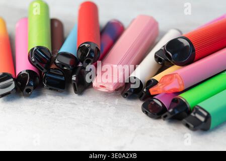 Collezione di varie sigarette elettroniche colorate monouso e penne vape sparse su sfondo grigio chiaro. Foto Stock