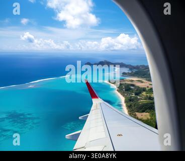 Vista aerea di una spiaggia tropicale catturata da un oblò di aeroplano, che mostra una prospettiva mozzafiato Foto Stock