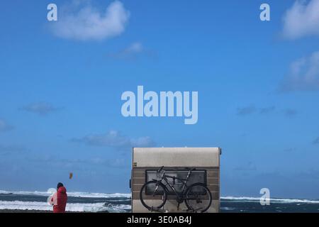 Vista sul retro di un vecchio camper con una bicicletta e una persona con una giacca rossa sulla spiaggia che si affaccia sul turchese Oceano Atlantico Foto Stock
