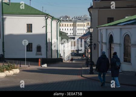 Minsk, Bielorussia - 8 marzo 2026: Strada in pendenza tra edifici storici con tetti verdi, pedoni che camminano lungo la strada acciottolata nella città vecchia Foto Stock