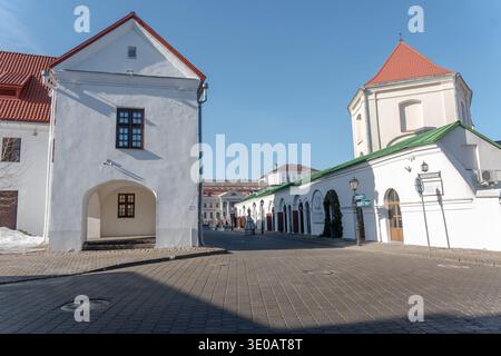 Minsk, Bielorussia - 8 marzo 2026: Edifici storici bianchi con tetti rossi e passaggi ad arco intorno alla piazza acciottolata nel quartiere della città vecchia di Minsk Foto Stock