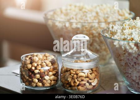 Ciotole di vetro con popcorn e vasetti con noci Foto Stock