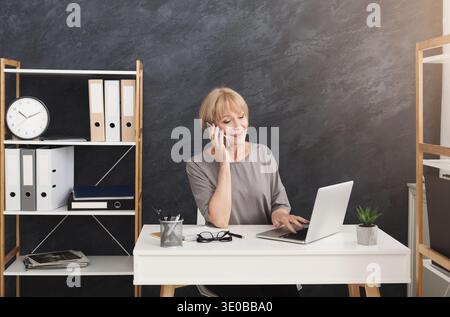 Felice donna d'affari di mezza età al lavoro che parla al telefono Foto Stock