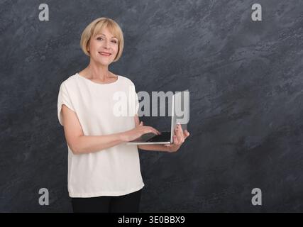 Donna matura in abiti casual con notebook su sfondo grigio Foto Stock