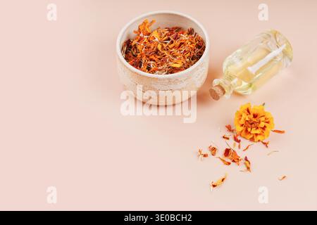 Petali Marigold e bottiglia di olio su sfondo beige Foto Stock