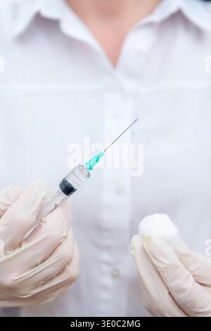Primo piano di mani del medico che tengono la siringa e il cotone prima dell'iniezione del vaccino, concetto di preparazione medica, procedura di immunizzazione e assistenza sanitaria tr Foto Stock