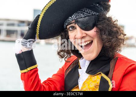 Donna vestita da pirata con un occhiello e un cappello tricorno, sorridendo e ridendo durante una divertente festa di carnevale, godendosi l'atmosfera festosa Foto Stock